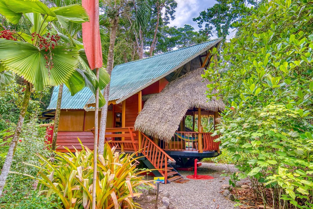 Flame-heated stone hot tub on the veranda beside the dining table, hammock and jungle beyond