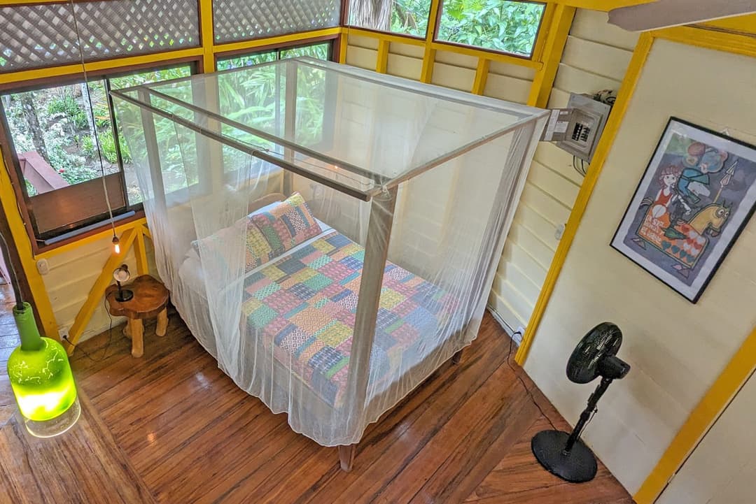 Downstairs queen bed under a full mosquito net, polished hardwood floor, fan, screened windows to the garden