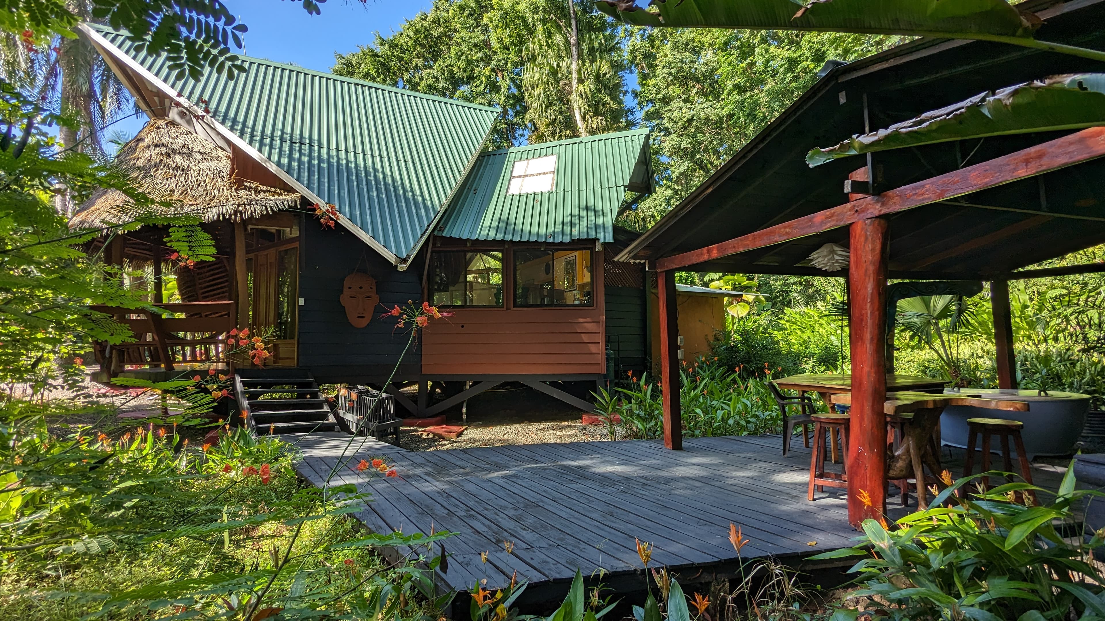 Beach House — full west face at golden hour, green metal roof and thatched eaves above the rattan-walled veranda